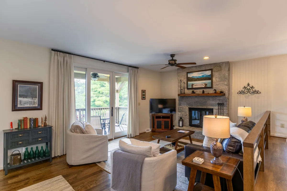 An inviting interior scene featuring a cozy fireplace, plush seating area, and expansive windows that open onto a balcony. The room bathes in natural light, suggesting easy access to the outdoors and relaxation after a day spent exploring the town.