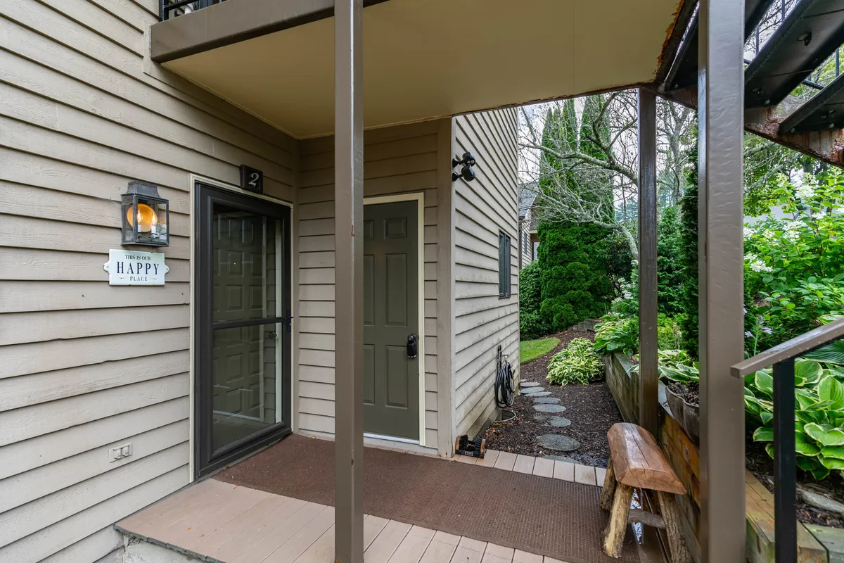The photo showcases a welcoming front door with a charming pathway surrounded by greenery. A 'welcome' sign and a bench offer a sense of hospitality and warmth, inviting guests to step outside and begin their adventures. The manicured landscaping hints at the proximity to nature and the town's inviting character.