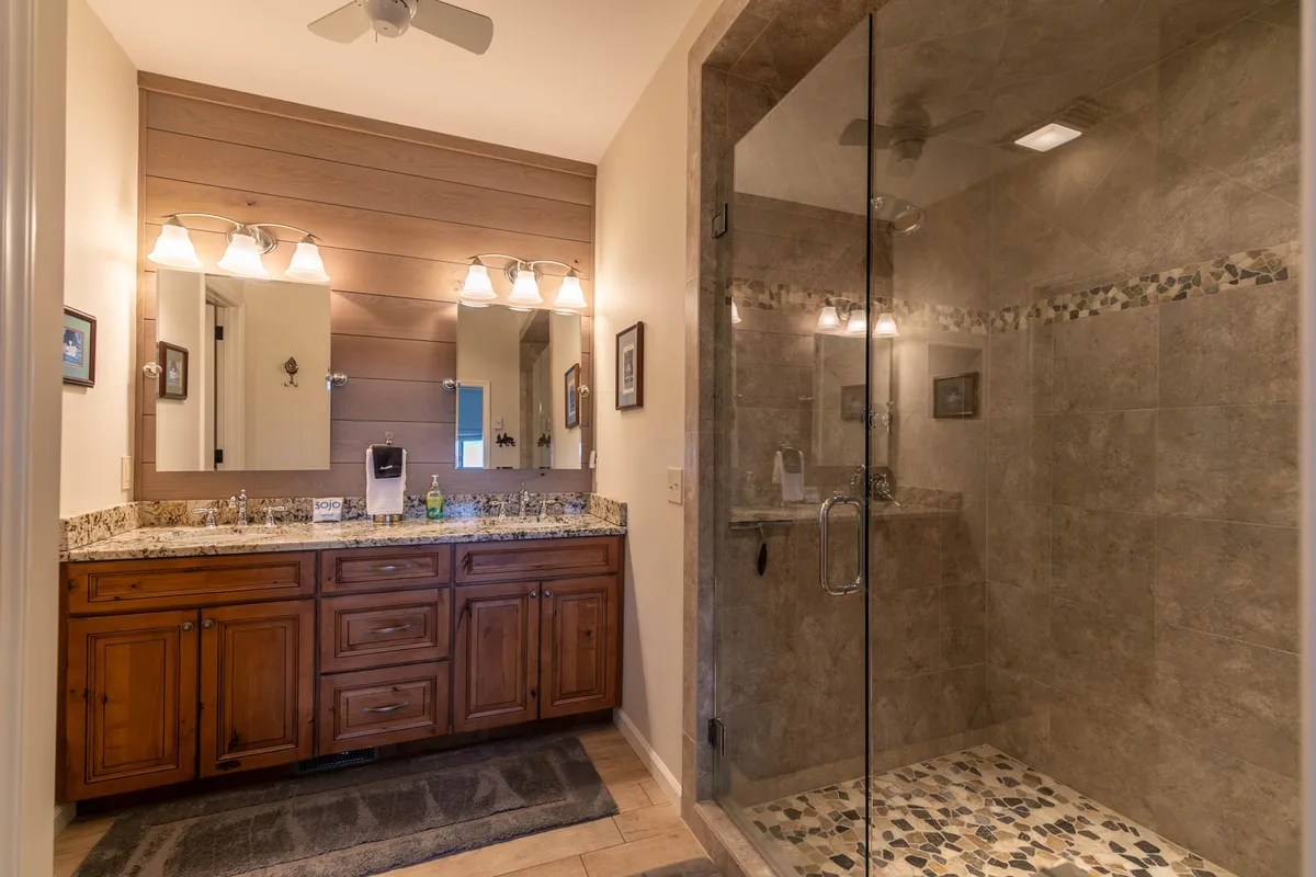 A serene bathroom retreat featuring a wooden vanity, granite countertop, glass shower, and decorative tile accents. The space radiates calm and is designed for self-care and relaxation after active days.