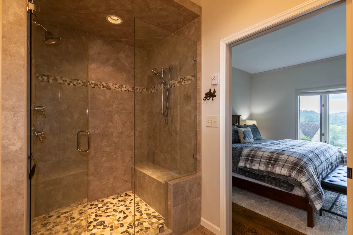 A spa-inspired ensuite bath showcasing a glass shower enclosure with beautiful stone tiles and a partial view into the adjacent bedroom. The ambiance is serene and tranquil, ideal for self-care and relaxation.