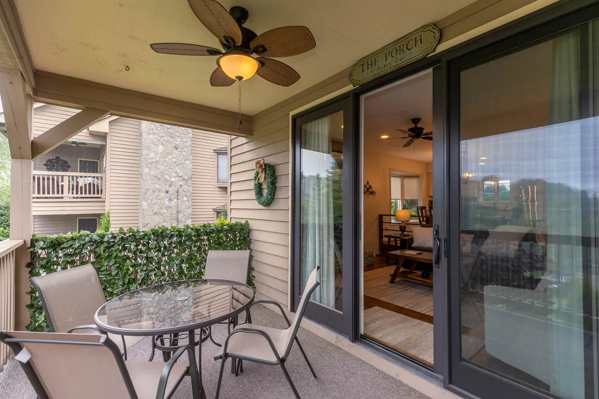 A welcoming patio featuring a table with chairs, a decorative wreath, and a view looking into the interior living space. The scene is bright, with natural light streaming through the windows, suggesting a peaceful spot to enjoy morning coffee or relax in the evening.