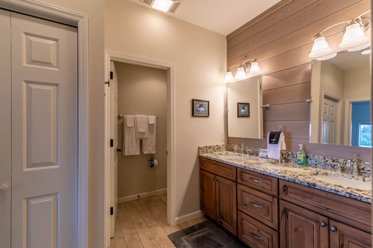 A bathroom with a double granite vanity, granite countertops, wood paneling accents, and framed pictures. The space is functional yet relaxing, perfect for morning routines or shared moments.