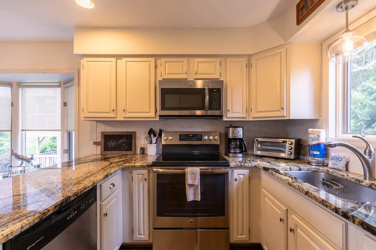 A bright and modern kitchen scene featuring sleek granite countertops, stainless steel appliances, and a window that bathes the space in natural light. The setup is designed for meal prep and casual gatherings, reflecting the gourmet amenities mentioned in the content.